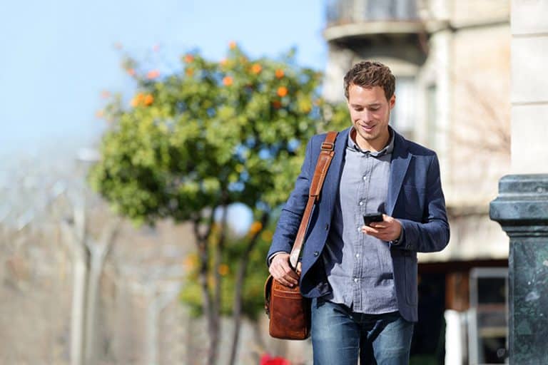 Young urban businessman professional on smartphone walking in st