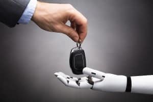 Close-up Of A Businessperson's Hand Giving Car Key To Robot On Grey Background
