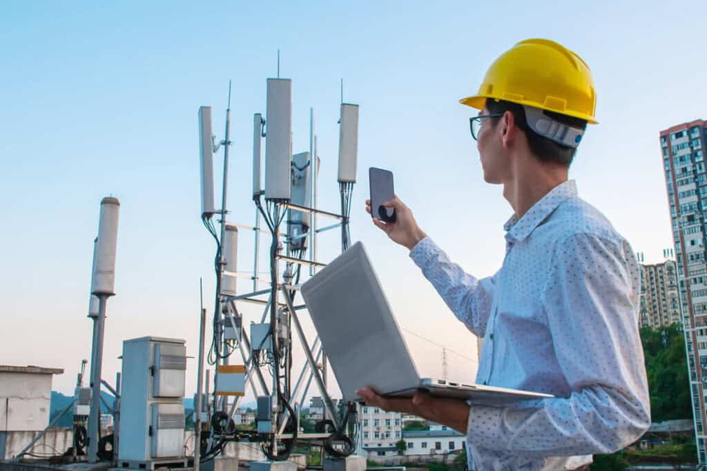 Engineer working on a laptop and phonechecking the communications