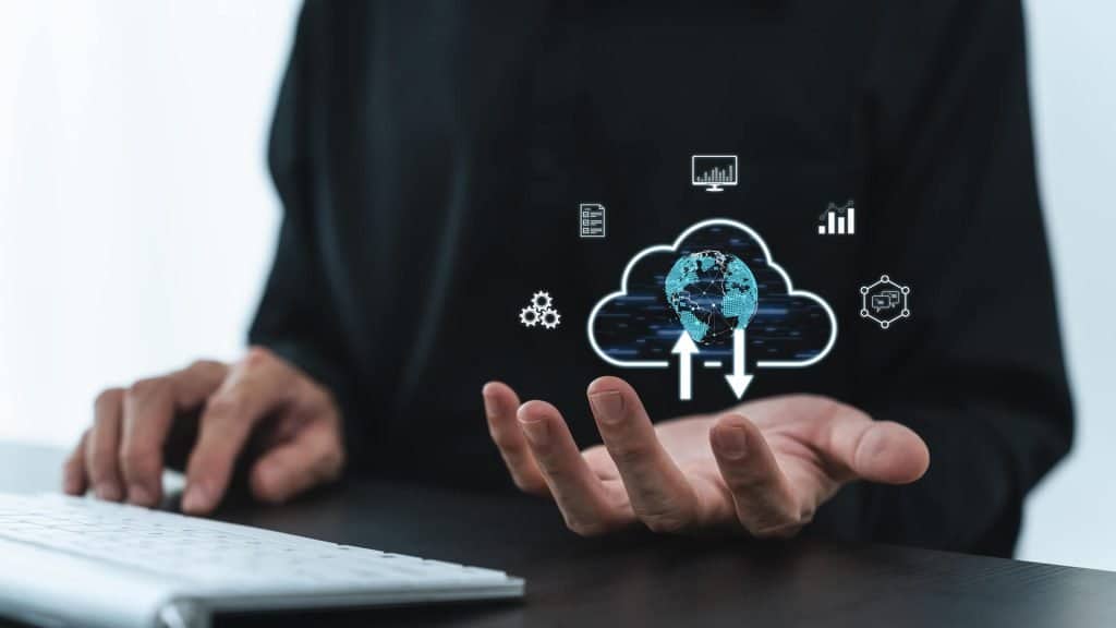 Photograph in which a section of a young man can be seen in front of a computer with one hand extended in front and upward in which, through illustration, a cloud was placed that represents a cloud managed service provider.