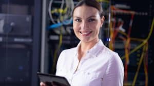 Image of a woman in a pink shirt holding a tablet while she stands in a server room, an image that illustrates what makes a top managed service provider.