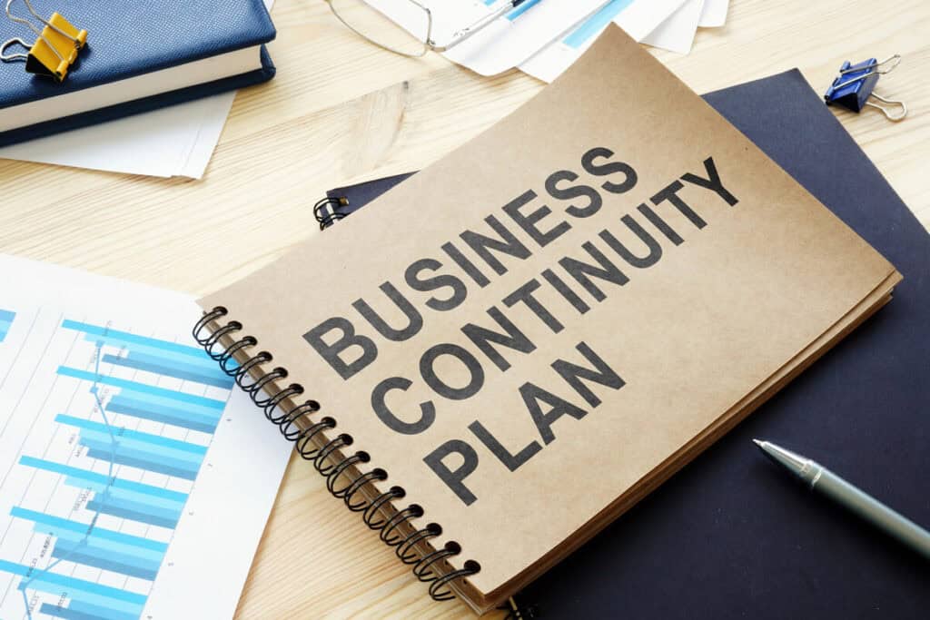 Spiral-bound book titled "Business Continuity Plan" on a desk with charts and a pen.