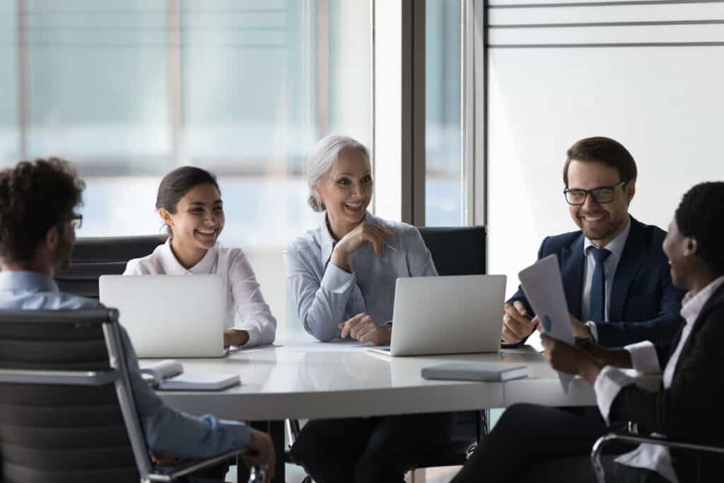 A diverse group of business continuity planning stakeholders in a meeting, discussing strategies and documents with laptops.