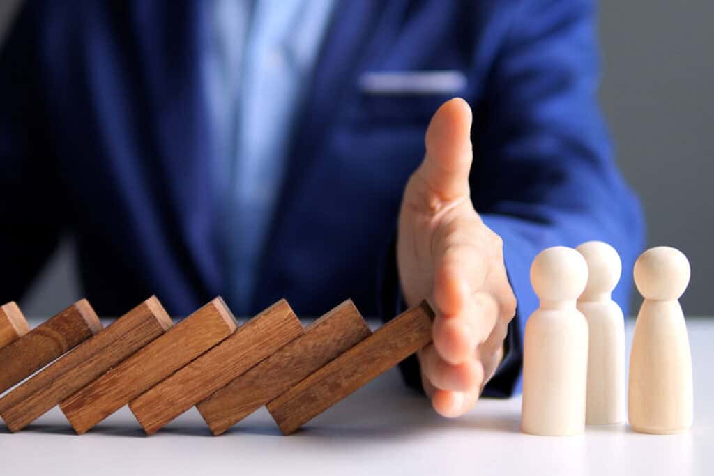 Businessman preventing domino effect, protecting wooden figures