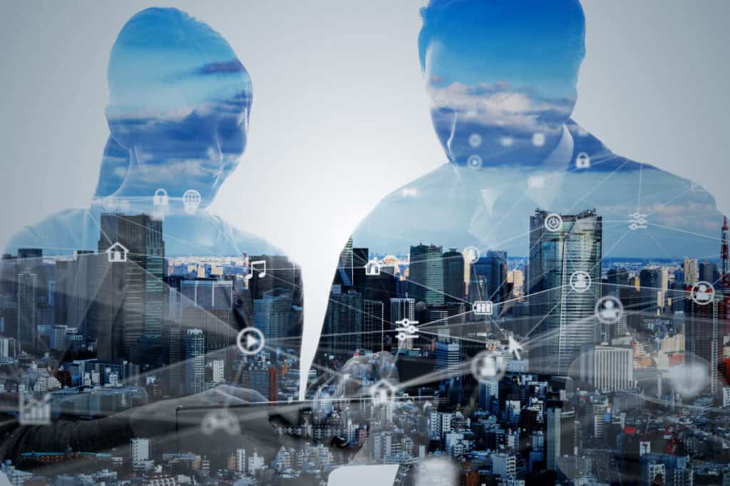 A double exposure image shows two people in a business setting, overlaid with a cityscape and interconnected digital icons. The scene represents the definition of disaster recovery, highlighting the integration of technology and urban resilience.