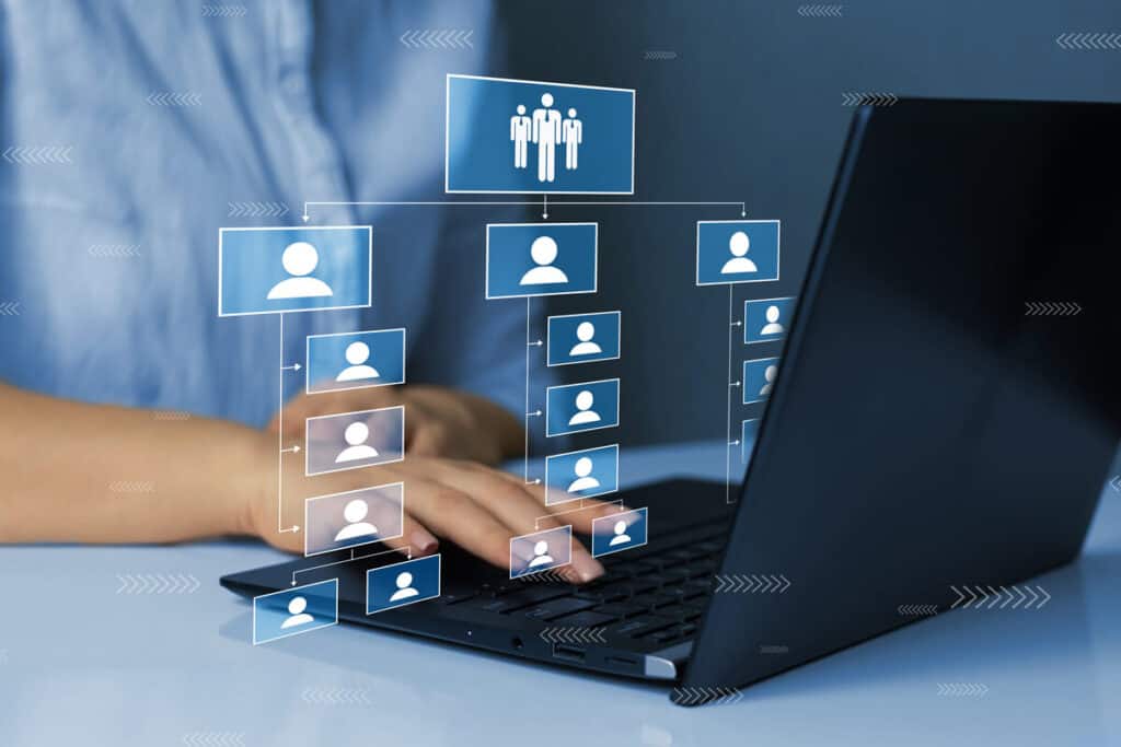 A person working on a laptop with a digital organizational chart overlay showing departmental responsibilities in BCP (Business Continuity Planning).