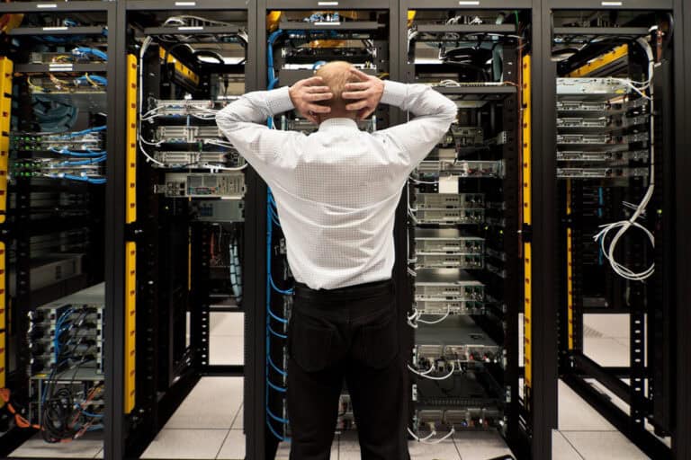 A man stands in a server room, holding his head in frustration, illustrating the difference between business continuity and disaster recovery.