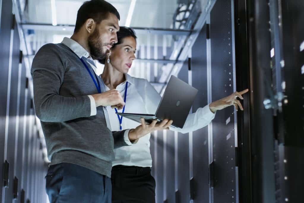 Two IT professionals inspecting servers in a data center, emphasizing technological resilience and infrastructure stability.