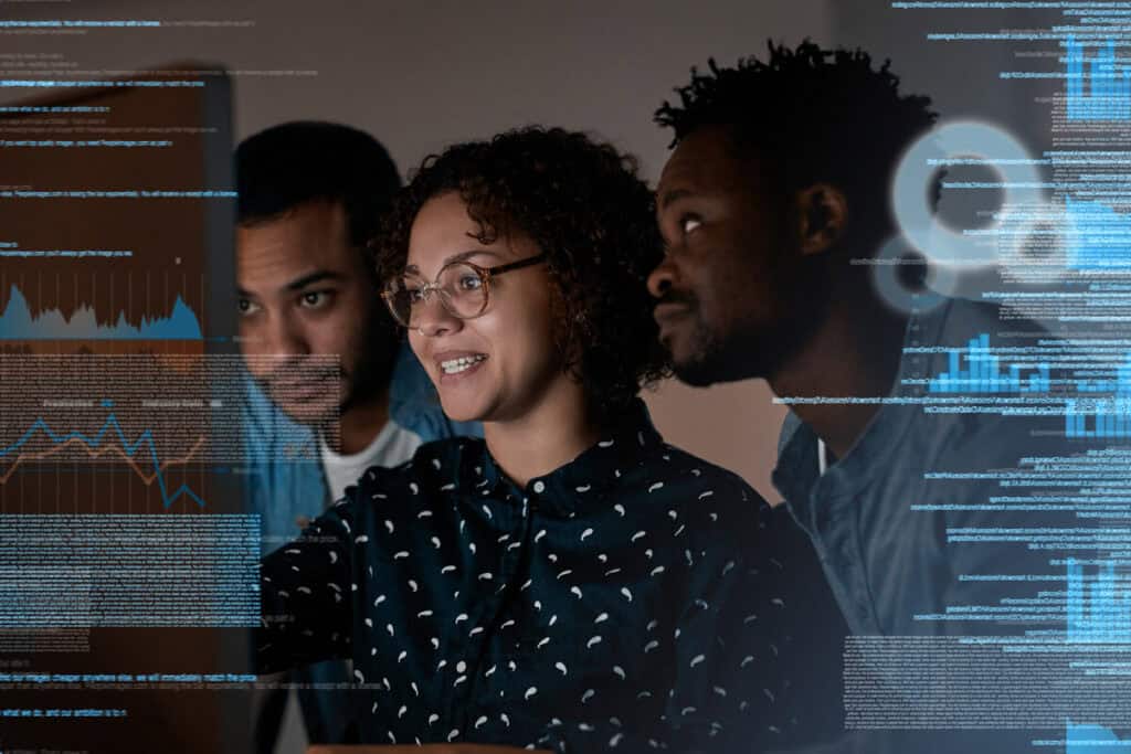 A diverse group of three colleagues examining data on a computer screen, illustrating collaboration and analysis. This image represents the teamwork involved in answering the question of who is responsible for business continuity plans.